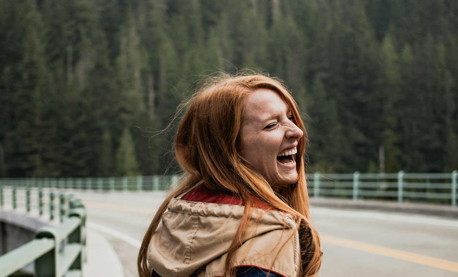 A woman laughing on an open road, hair caught by the wind