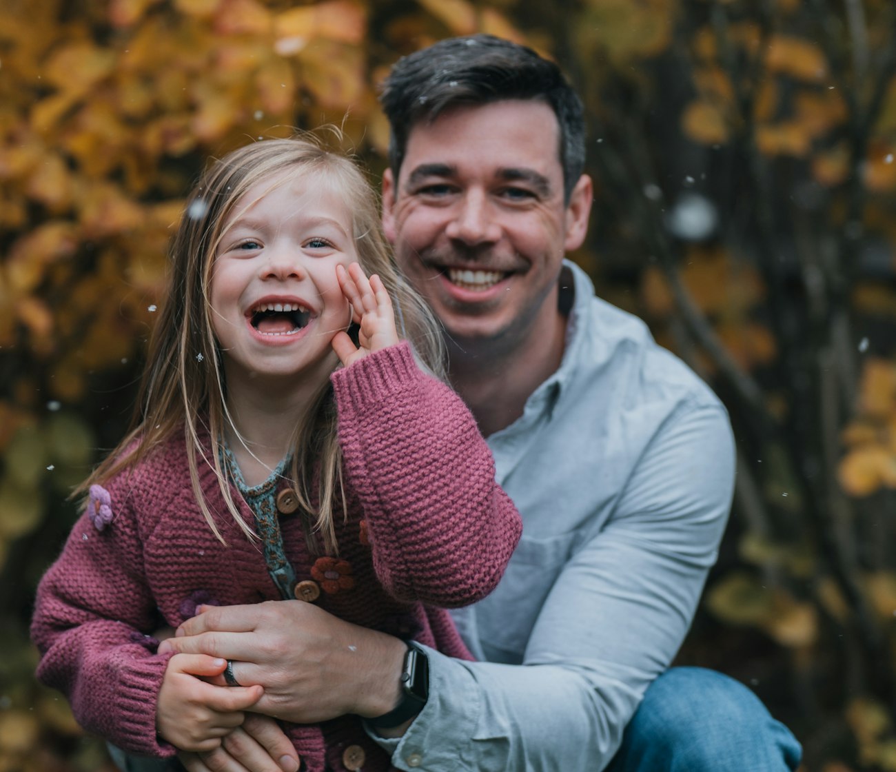 A father and his daughter laughing together outdoors in autumn light