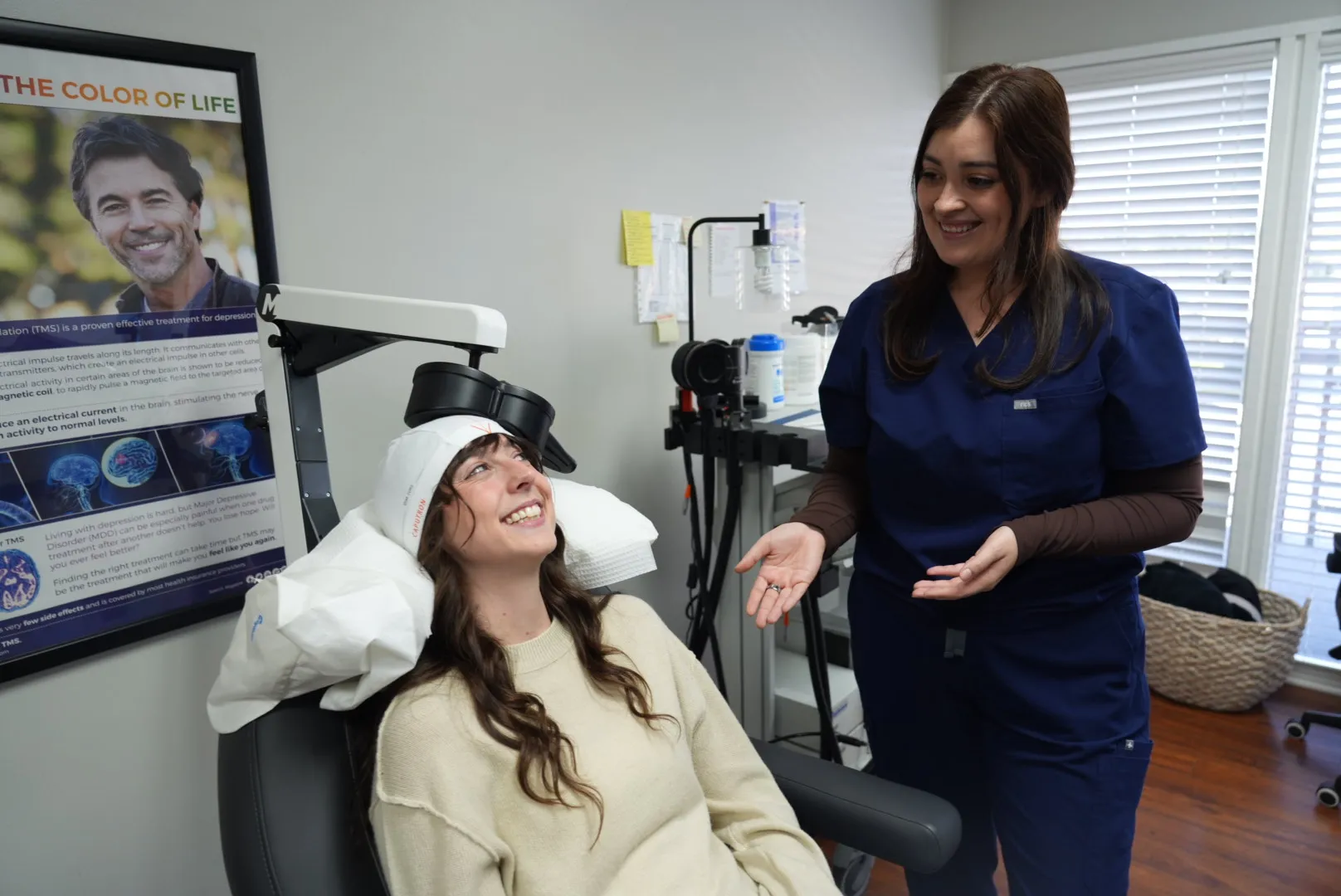 A smiling patient in the TMS chair, coil positioned, with a clinician talking her through the session