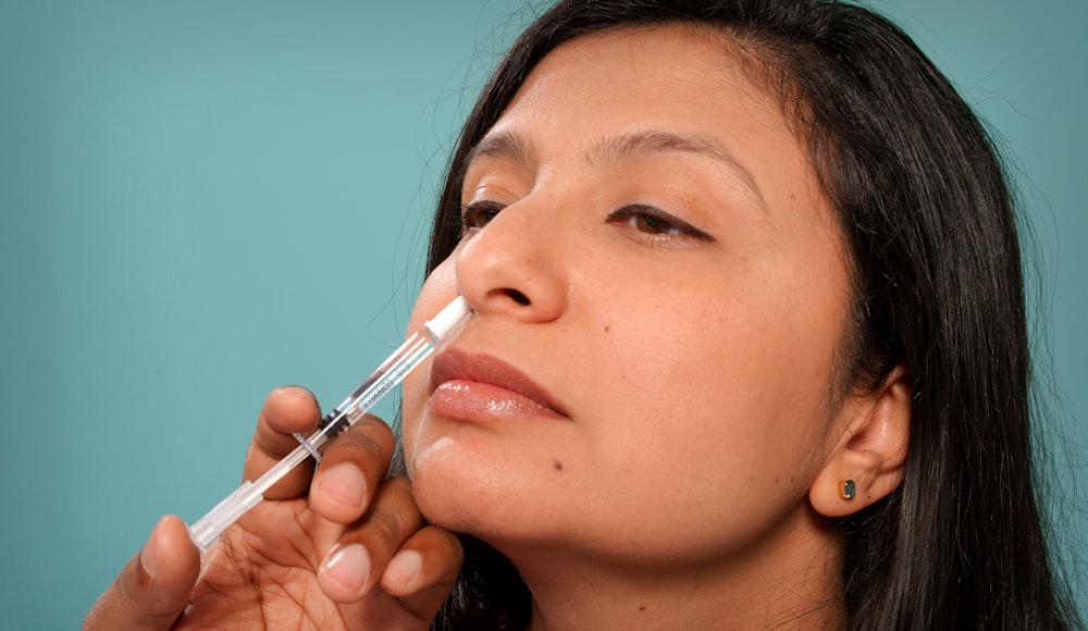 A person self-administering a nasal spray
